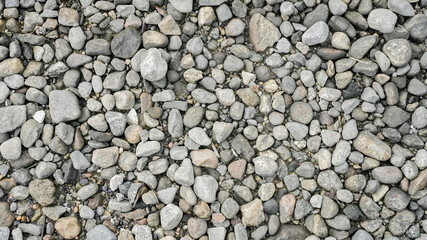 A close-up view of various smooth stones arranged naturally on the ground in a gravel area under natural light