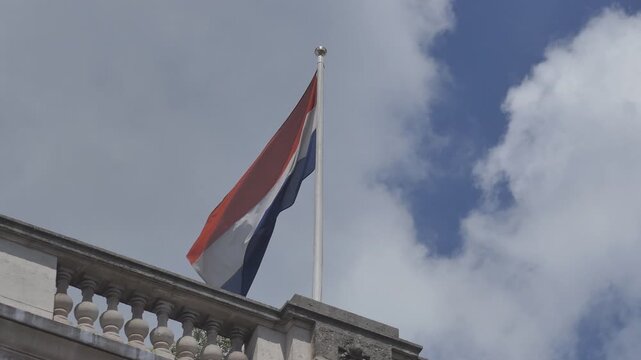 A flag of Netherlands waving on a building rooftop.
