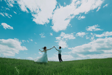 A couple dancing on a green hill under a bright blue sky with clouds, capturing a moment of joy and freedom in nature, with ample copy space.