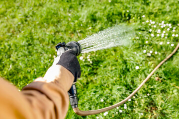 Gardener with watering hose in garden. Close - up of woman gardener hand in  brown garden suit...