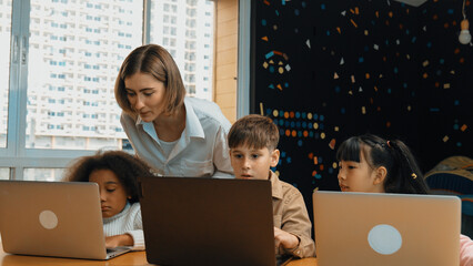 Smart teacher teaching and looking student using laptop at classroom. Professional instructor...