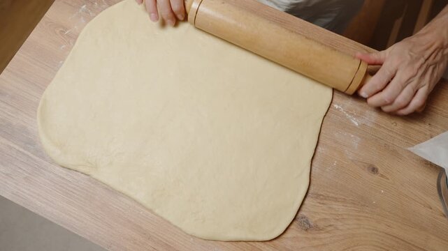 Flattening Dough into a Large Rectangle with a Wooden Rolling Pin, Ensuring Even Thickness.
