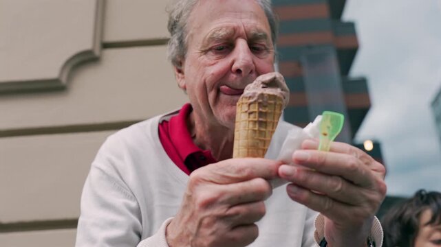 Older man enjoying a bite of his chocolate ice cream cone outdoors, relishing the flavor in a casual and relaxed moment of indulgence and simple pleasures