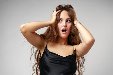 Fototapeta premium Young Woman in Black Slip Dress Looks Shocked in Studio Portrait