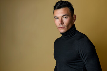Fototapeta premium A poised male model displays an air of confidence while showcasing a stylish look against a warm, golden background in a studio setting.