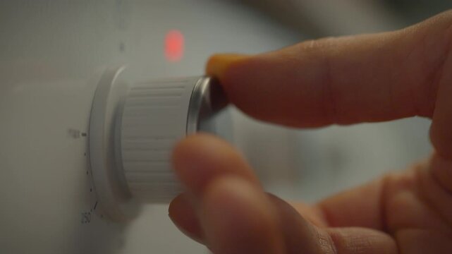 Close up of a male householder switching oven controls while cooking dinner in a home oven. Cooking food in an oven. Close up of temperature control switches on the control panel