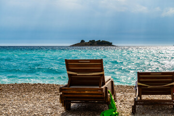 Lounge chairs folded on the beach edge in the small town of Rogoznica, Croatia, looking on the open sea and small island on the horizon