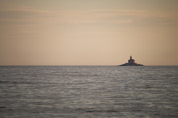 Obraz premium Stone lighthouse Mulo far on the horizon in front of small tourist town of Rogoznica, Croatia
