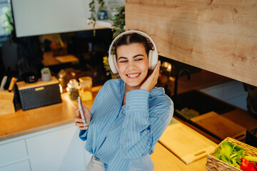 Young caucasian woman singing and listening to music in kitchen