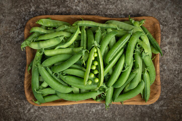 Green peas in a wooden plate on a dark background. Fresh green peas in pods. View from above.