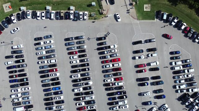 Full parking lot of electric, gas vehicles with people walking, cars driving around looking for available spot, parallel pattern, pavement marking number in metropolitan Arlington, Texas, flyover. USA