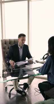 Young woman applicant get hired sit at desk, shaking hand, express respect to male HR manager finish job interview successfully in office, vertical view. Human resources, company staffing, headhunting