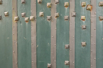 A close up of a weathered green wooden door with metal accents The door is adorned with square shaped metal studs adding a touch of rustic charm