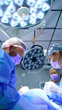 Two cooperating diverse doctors perform surgery on thyroid. Low angle view at the doctors carrying out operation. Vertical video.