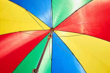 A vibrant and colorful beach umbrella viewed from below, showcasing the bright hues of red, yellow, blue, and green against a clear sky.