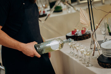Waiter pouring martini or champagne in crystal glasses on table party at wedding reception