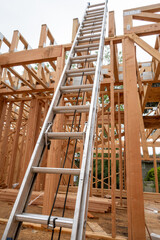 Interior new house construction at wood framing stage, aluminum extension ladder propped up on 2nd floor support truss beams
