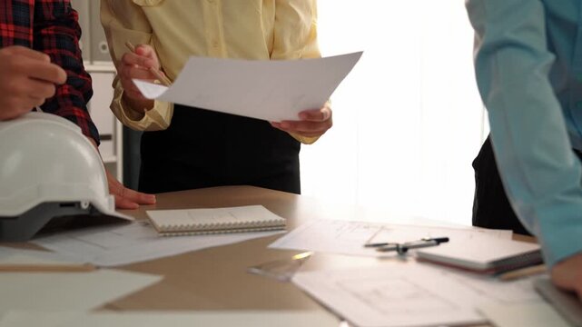 Architect and safety engineer discussion about building blueprint displaying on laptop on table with architectural document and wooden block scatter around at modern office. Closeup. Delineation.