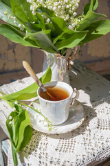 cozy still life with breakfast, hot tea in an antique porcelain cup and a bouquet of lilies of the valley in an antique vase,
