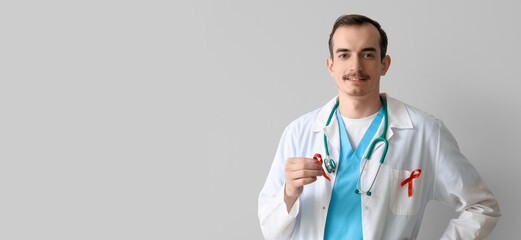 Young male doctor with red ribbons on grey background. AIDS awareness concept