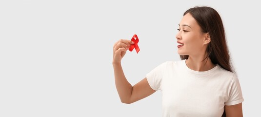Young woman with red ribbon on light background. AIDS awareness concept