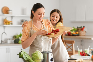 Little girl with her mother putting cut apple into blender in kitchen