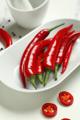 Plate with fresh chili peppers on light background
