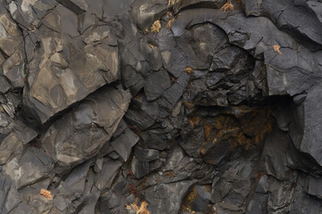 Dark grey rock face with many cracks and crevices forming an abstract natural pattern