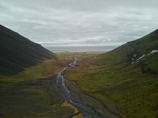 River flowing between two mountains leading to the ocean on a cloudy day