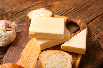 Board with processed cheese, bread and garlic on brown wooden background