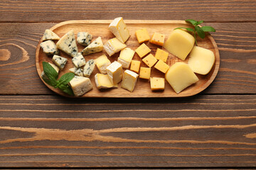 Board with pieces of tasty cheese on wooden background