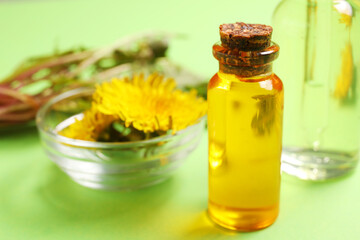 Bottles with cosmetic oil and bowl of dandelion flowers on green background