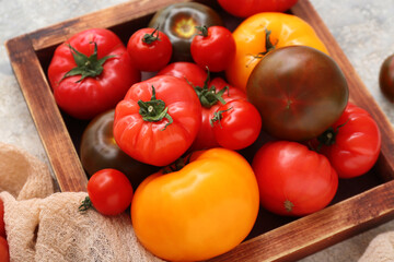 Wooden box with different fresh tomatoes on grey background, closeup