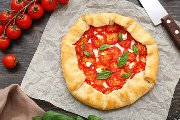 Baking paper with tasty tomato galette and basil on wooden background