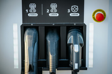 A close up view of three different electric vehicle charging connectors at a charging station,...