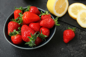 Bowl with ripe strawberry and lemon on dark background, closeup