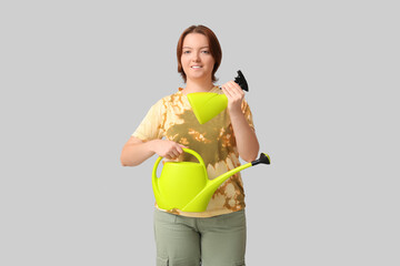 Smiling woman with watering can and spray bottle on grey background