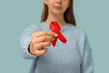 Woman holding red ribbon on blue background, closeup. World AIDS Day concept