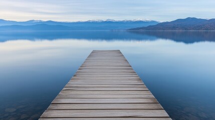 Fototapeta premium An old, weather-beaten wooden pier jutting into a tranquil lake, coarse textures highlighted by morning light, with mountains in the distance