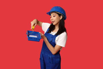 Female Asian painter with roller and tray on red background