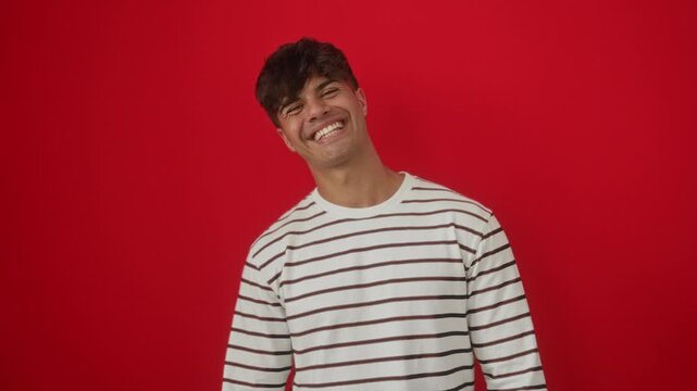 Young hispanic man wearing stripes t shirt standing with tongue out showing funny happy expression, sticking tongue out over isolated red background full of fun emotion