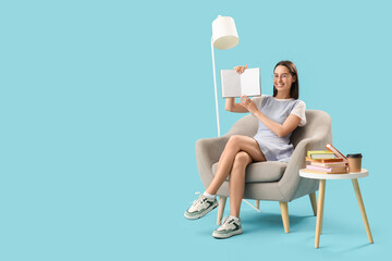 Young woman with book sitting in armchair on blue background