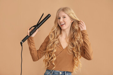 Beautiful young happy woman with curling iron on brown background