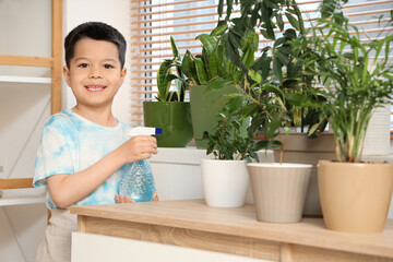 Cute little Asian boy watering houseplant near window in living room
