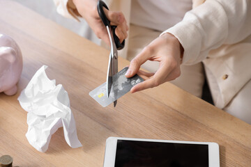 Bankrupt young woman cutting credit card at home, closeup