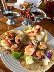 Traditional Mexican tacos with shrimp on corn tortillas at a Mexican restaurant, served with three types of sauces and nachos. Aesthetic serving on a wooden table