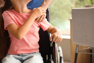 Little girl in wheelchair with nurse holding hands at home, closeup