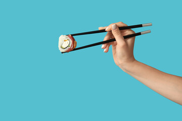 Female hand holding chopsticks with tasty sushi roll on blue background