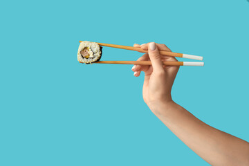 Female hand holding chopsticks with tasty sushi roll on blue background