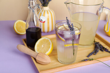 Glass and jug of fresh lavender lemonade with flowers and wooden juicer on colorful background